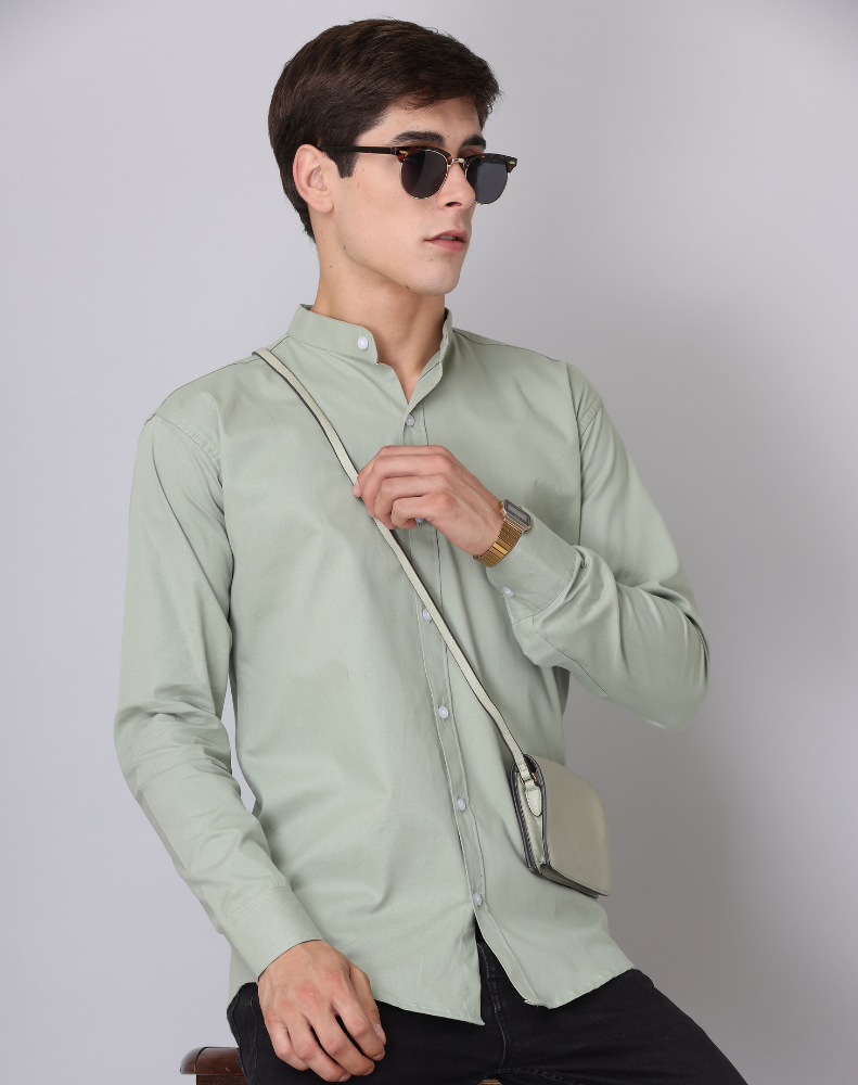 Man wearing a light green shirt and sunglasses, holding a small crossbody bag against a plain background