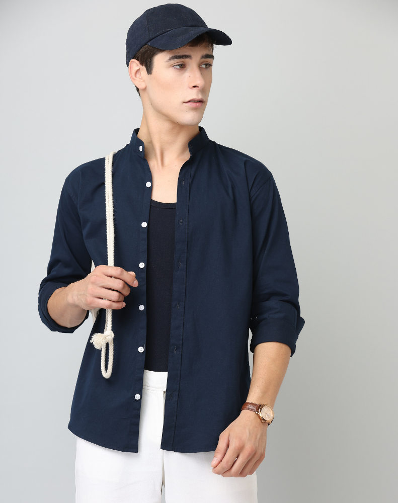 Man wearing a navy jacket, black shirt, and white pants against a gray background