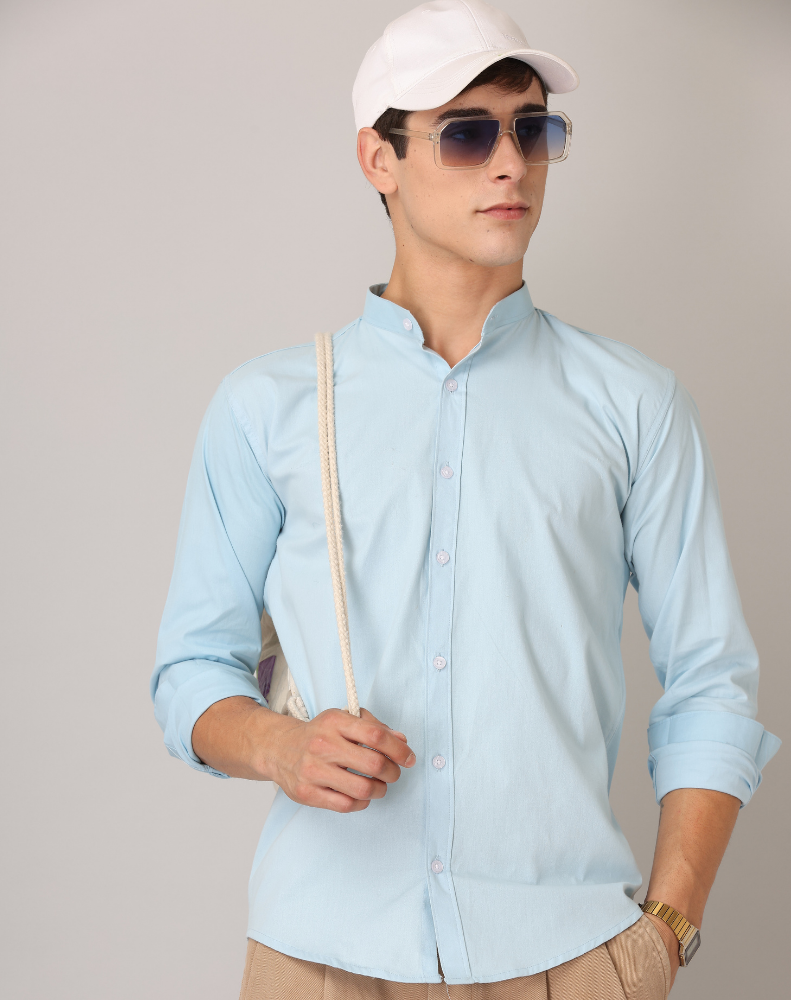 Man wearing a light blue shirt, beige pants, white cap, and sunglasses against a plain background