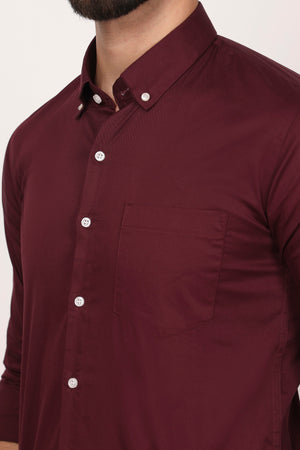 A person wearing a maroon-colored casual shirt with down buttons and a collar.