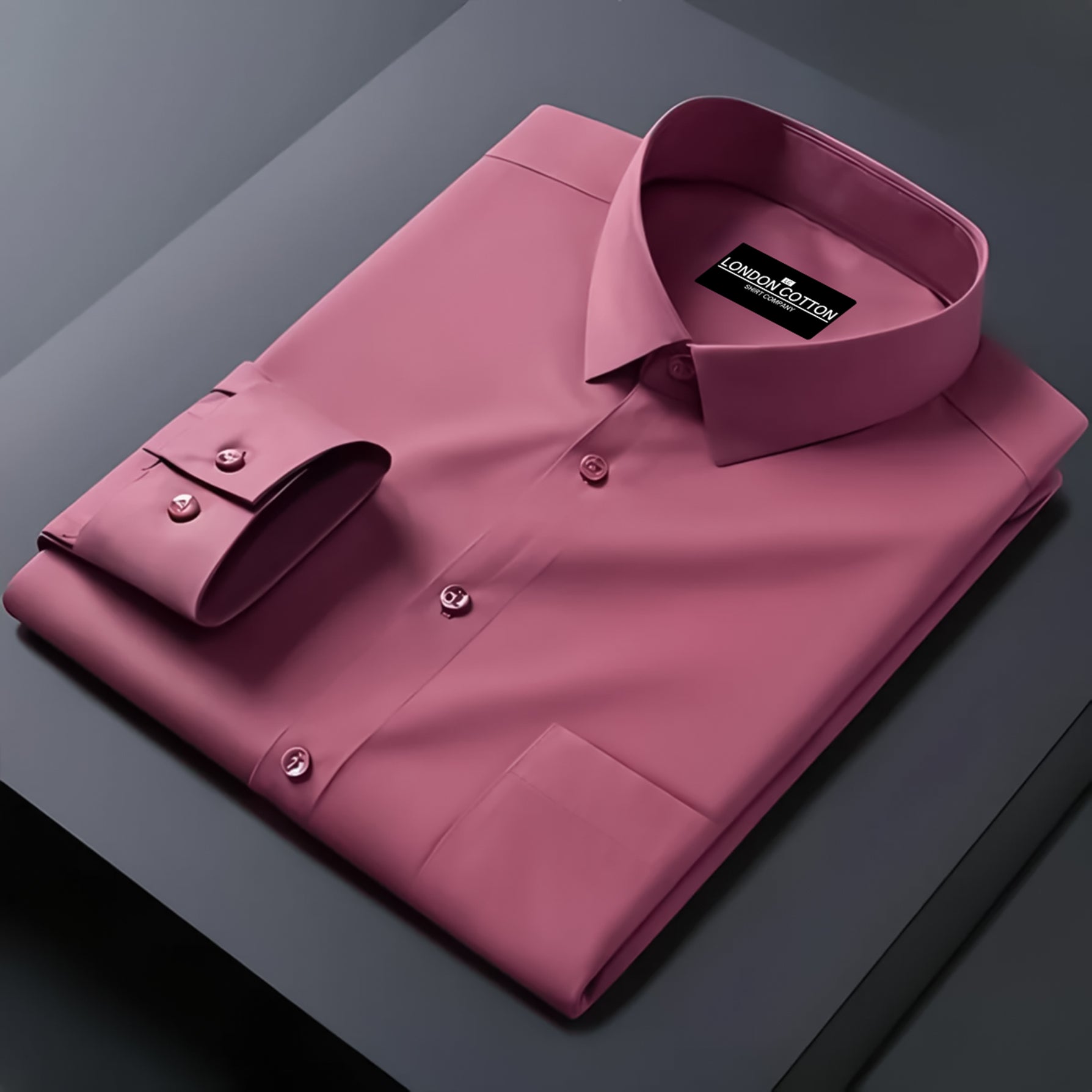 Folded pink dress shirt with a brand label on a dark surface